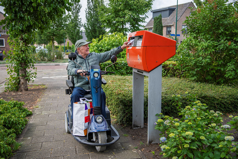 Foto: man op scootmobiel bij brievenbus