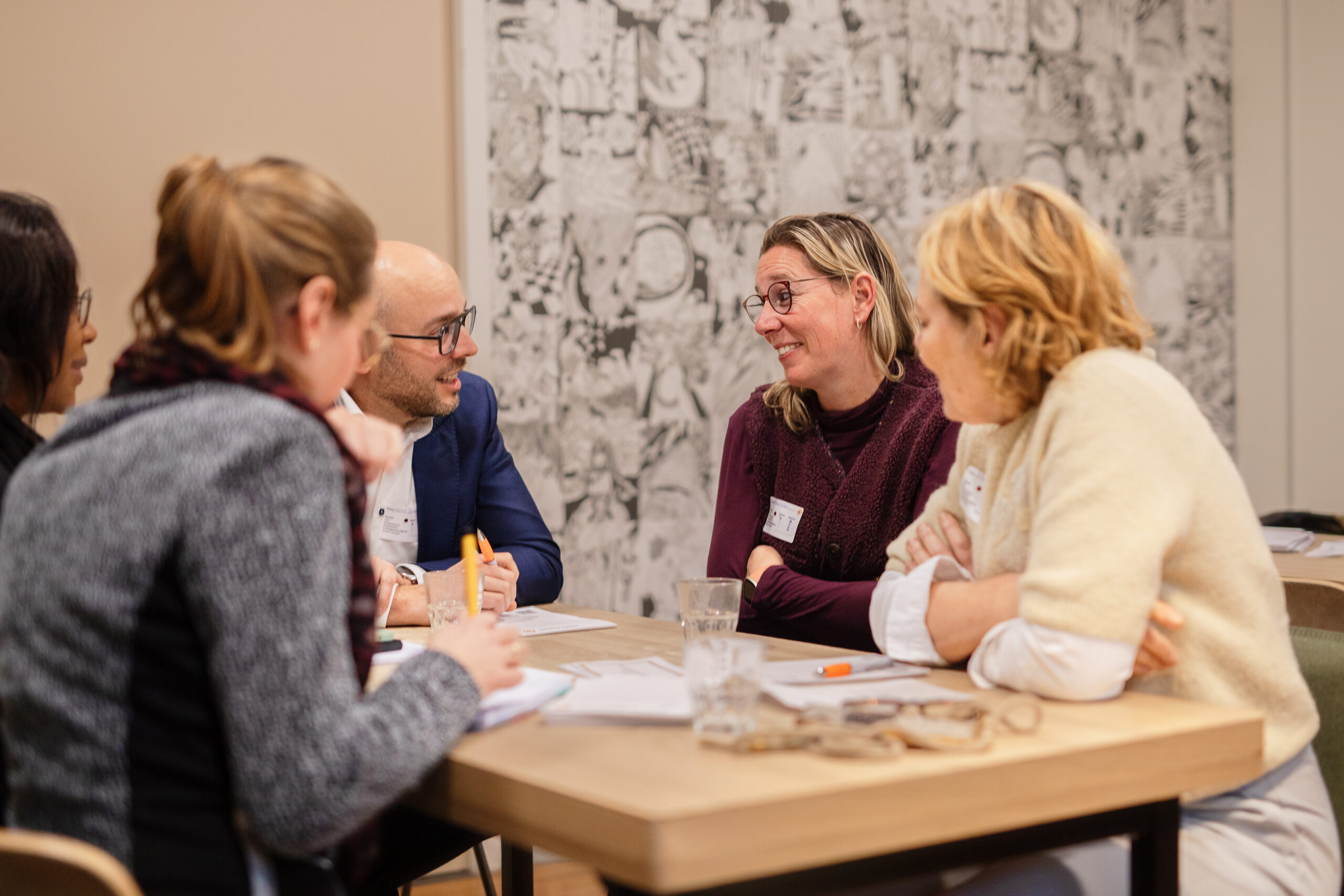 Mensen overleggen aan een tafel, er is contact. Ze spreken over het mentaal gezondheidsnetwerk